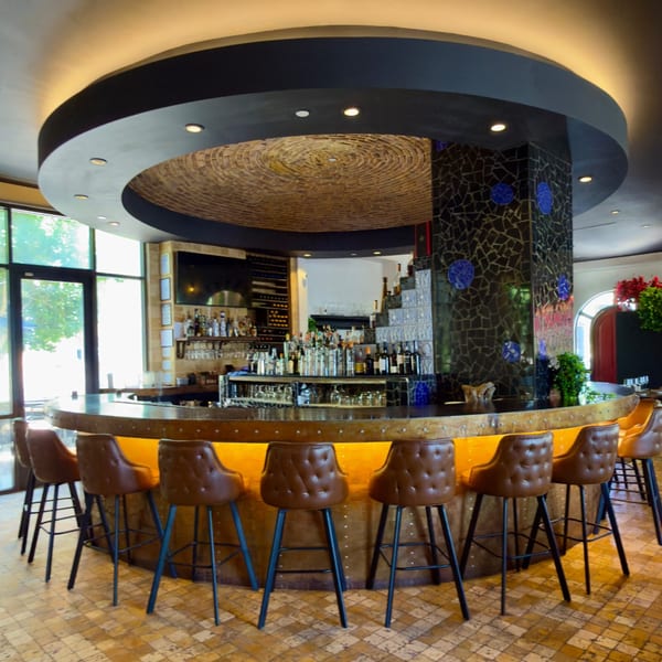 A circular bar with brown leather stools, a fully stocked liquor shelf, and a tiled ceiling.