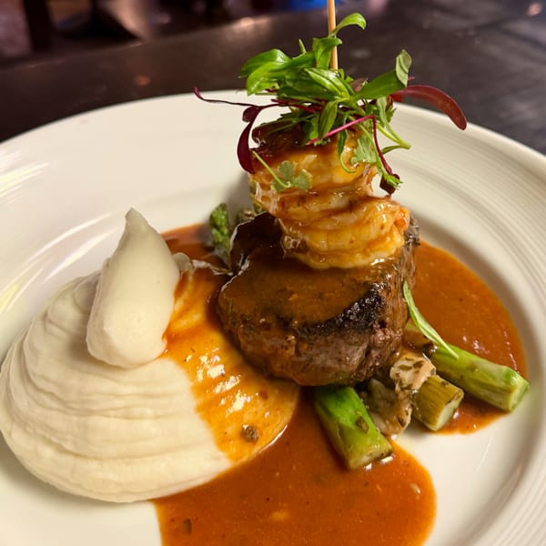 Filet mignon topped with shrimp and microgreens, served with mashed potatoes, asparagus, and sauce.