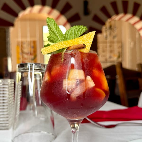 A glass of red sangria with fruit, mint, lemon peel, and a cinnamon stick.