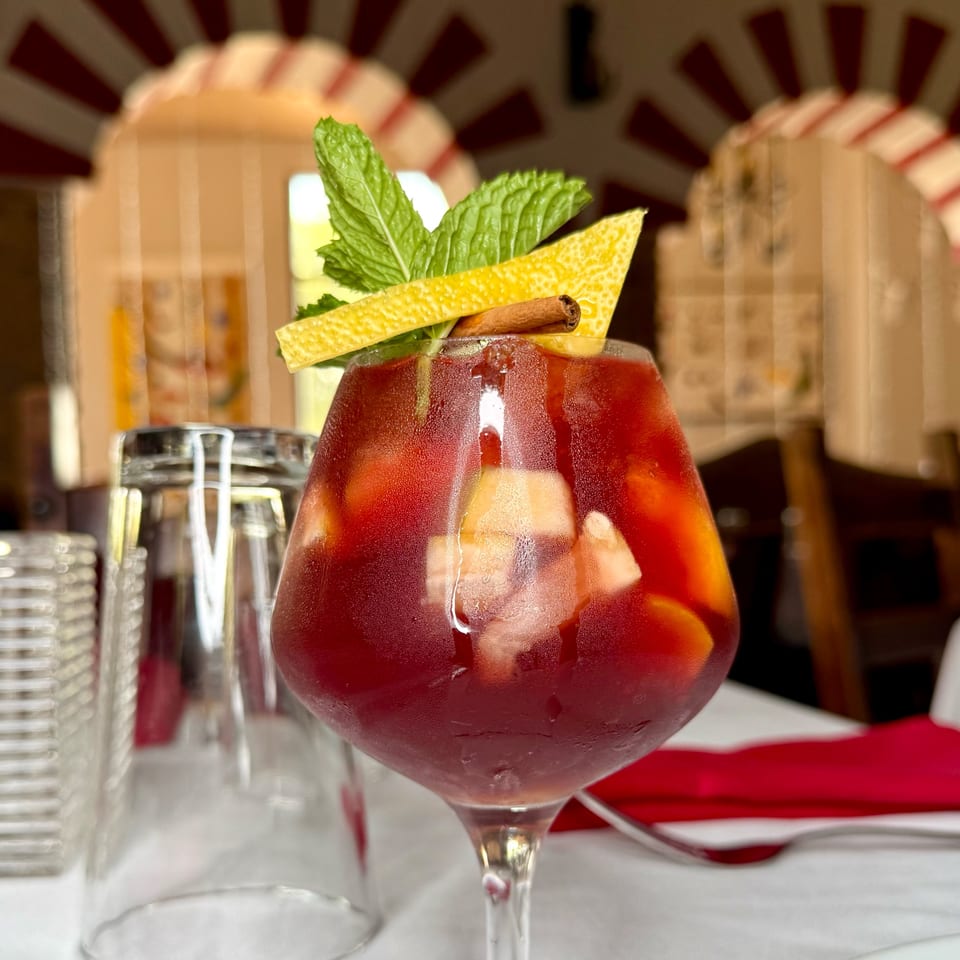 A glass of red sangria with fruit, mint, lemon peel, and a cinnamon stick.