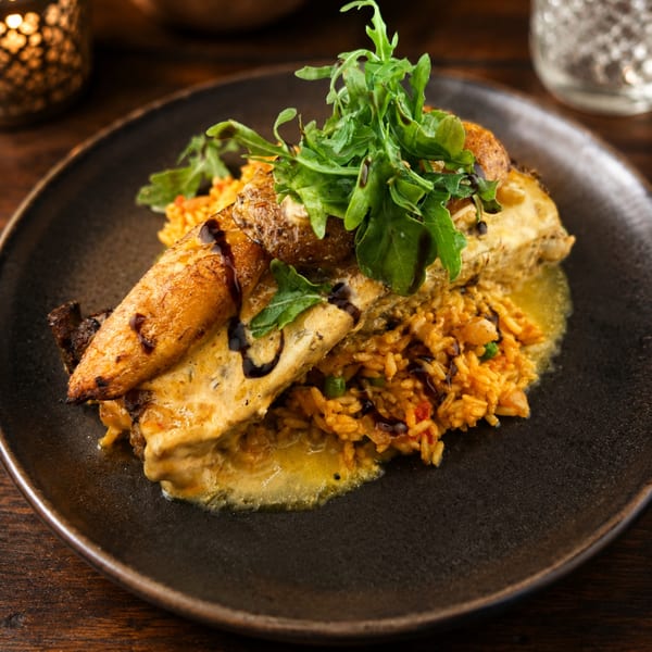 Roasted chicken and vegetables served over seasoned rice, topped with fresh greens and drizzled sauce on a dark plate.