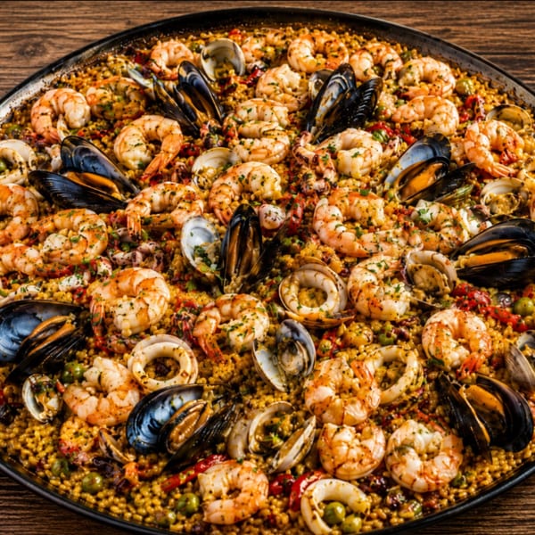 Close-up of a large paella pan filled with seafood paella, featuring shrimp, mussels, clams, and calamari.