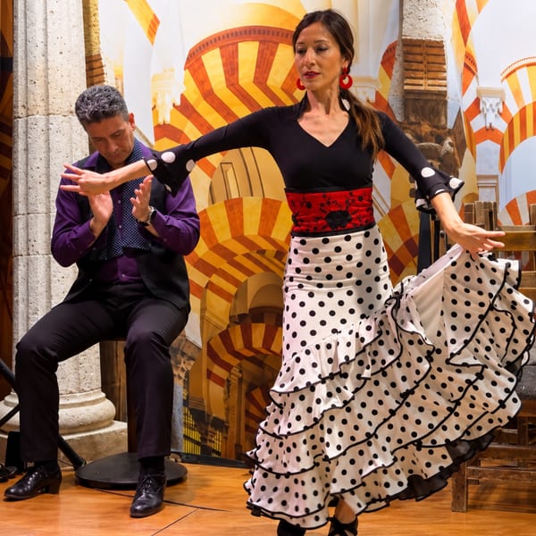 Flamenco dancers perform in ornate costumes before a colorful Spanish architectural backdrop.