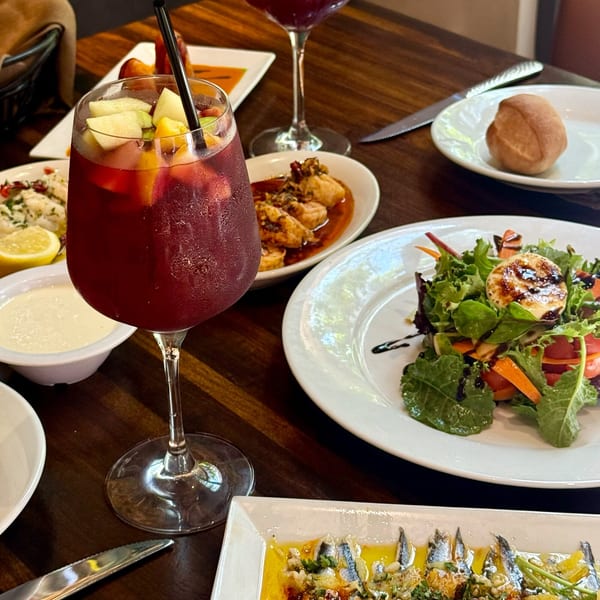 A table laden with various tapas dishes, including a salad, sardines, and a glass of sangria.