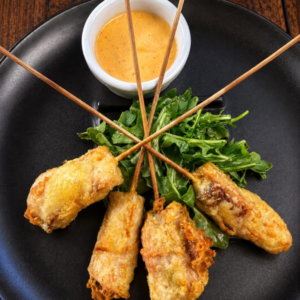 Golden fried appetizers with fresh greens and creamy dipping sauce arranged on a black plate.
