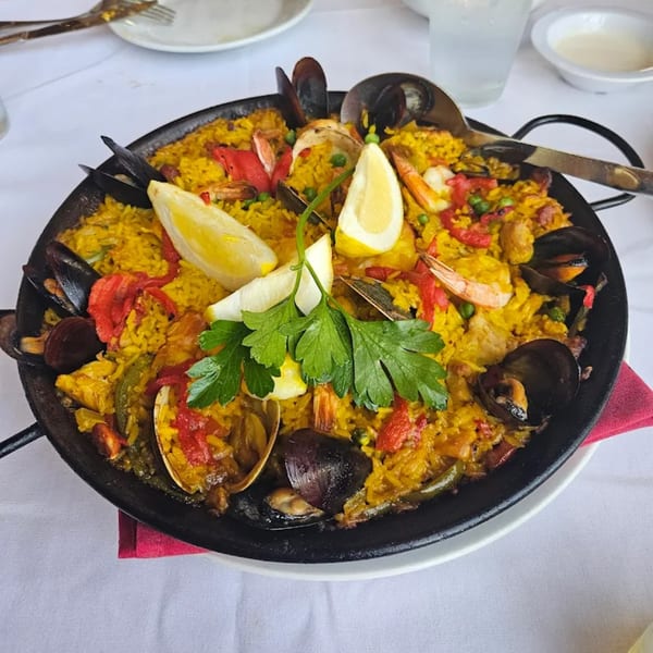 A large Spanish seafood paella in a black pan, garnished with lemon wedges and parsley.