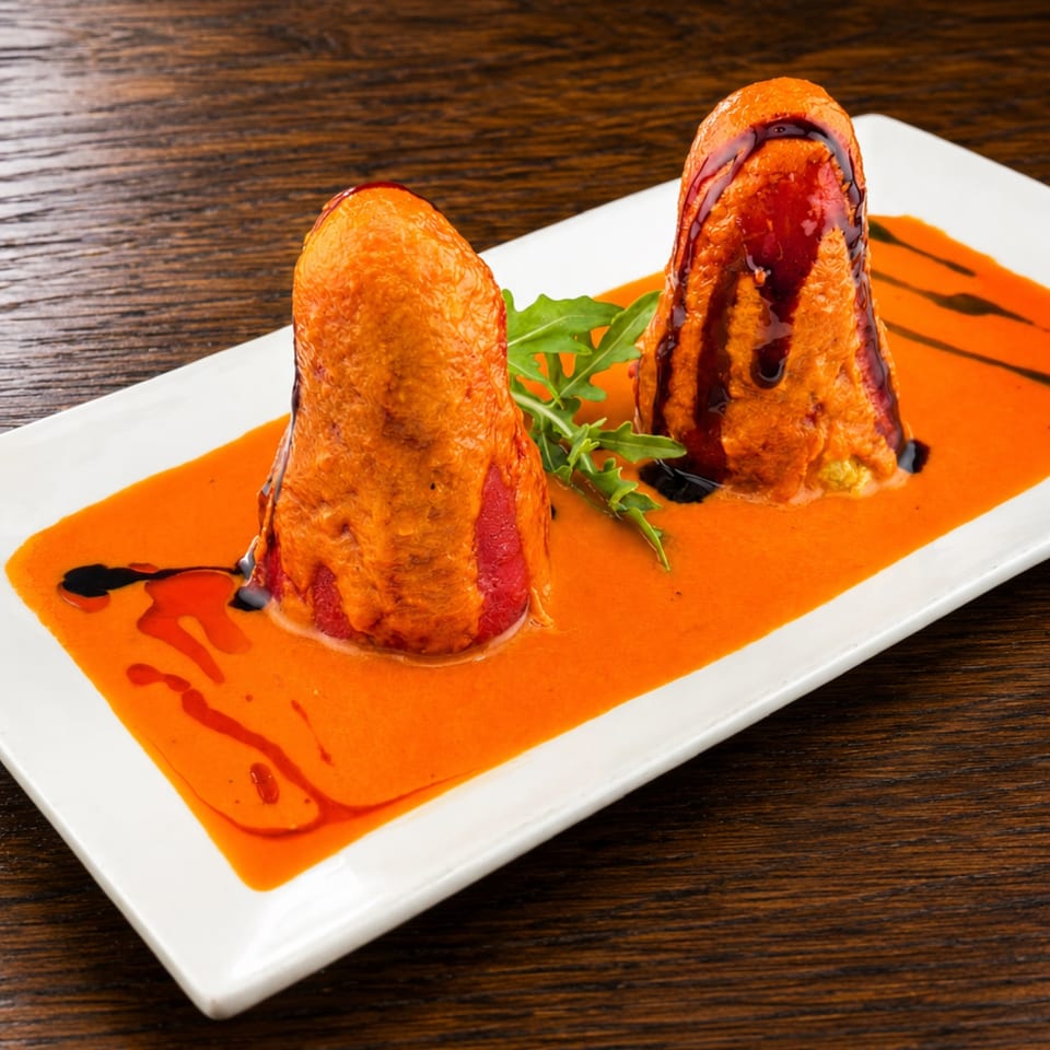 Two fried, sauce-drizzled appetizers sit on a white rectangular plate with orange sauce, balsamic glaze, and arugula.