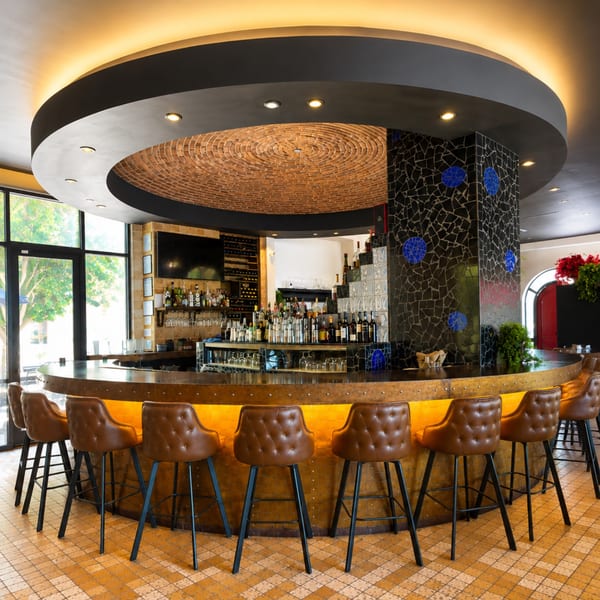 Elegant restaurant bar with brown leather stools, liquor bottles, mosaic tile accents, and a dramatic circular brick ceiling.