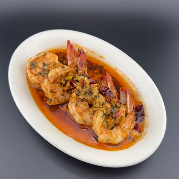 Shrimp scampi in a white oval dish, garnished with herbs and chili flakes.