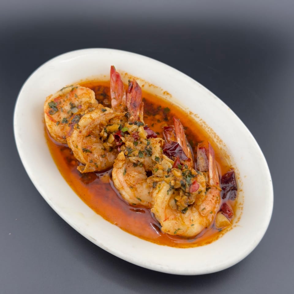 Shrimp scampi in a white oval dish, garnished with herbs and chili flakes.