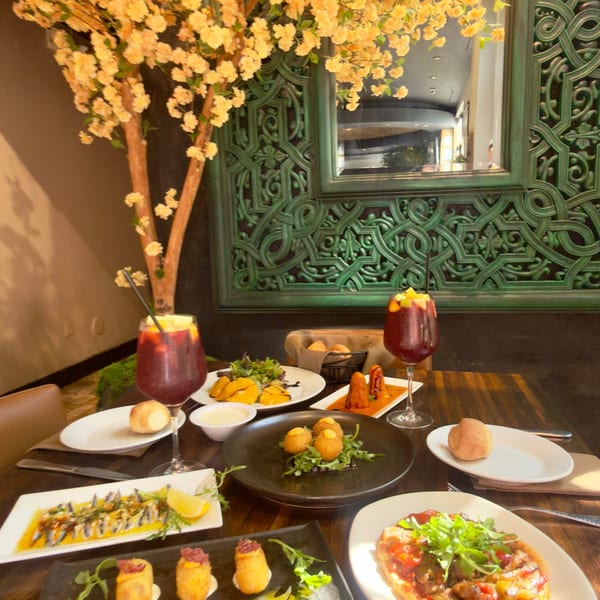 A table laden with various tapas dishes and two glasses of sangria, under a decorative tree.