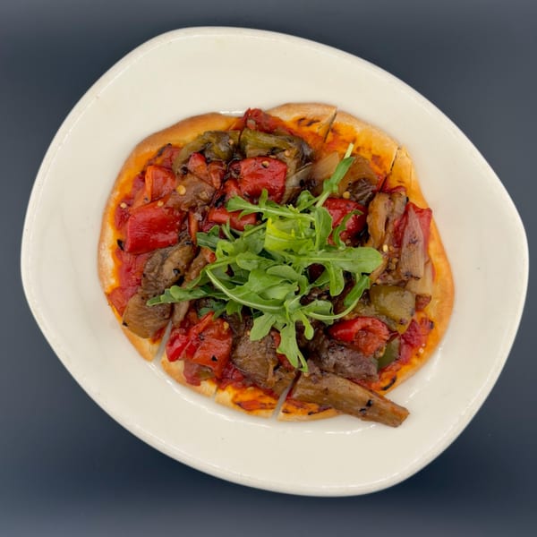 Flatbread pizza topped with roasted red peppers, green peppers, onions, and arugula on a white plate.