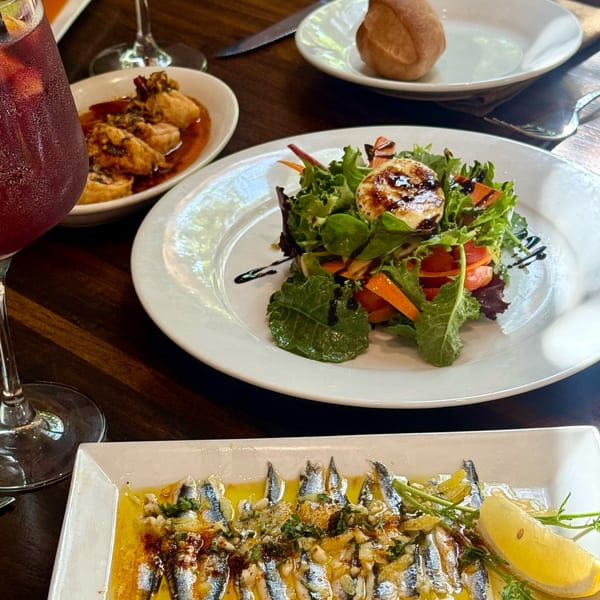 A table laden with Spanish tapas: sangria, shrimp, a salad with goat cheese, and sardines.
