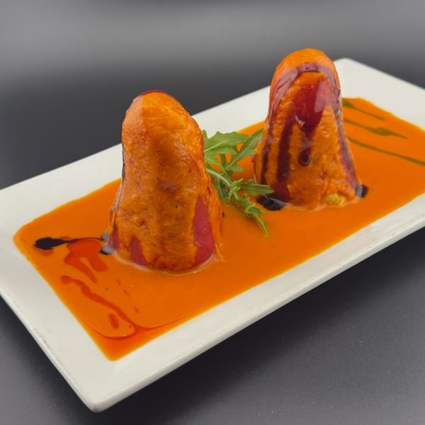 Two red peppers covered in orange sauce and drizzled with dark balsamic glaze on a white plate.