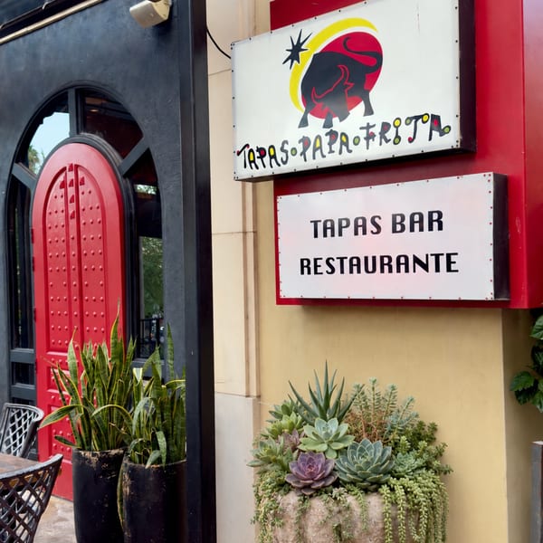 Tapas Papa Frita restaurant exterior with a red door, signage, and potted plants.