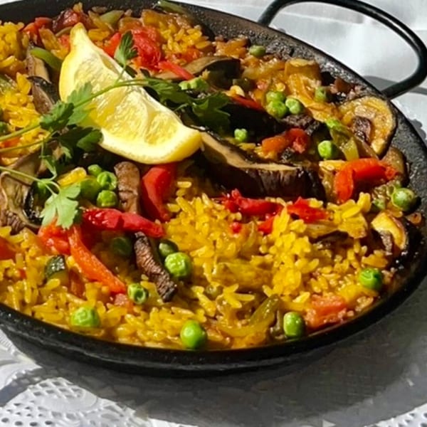 Vegetable paella in a black pan, garnished with a lemon wedge and parsley.