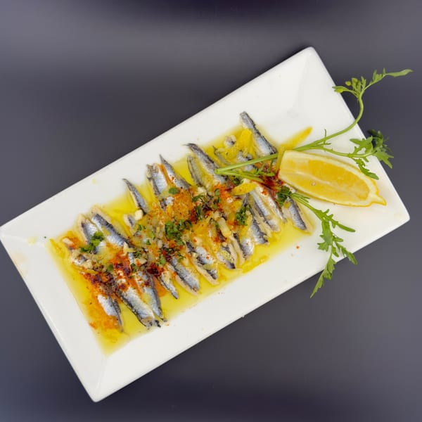 Marinated anchovies with lemon, herbs, and spices on a white rectangular plate.