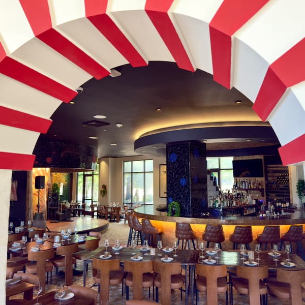 A restaurant interior with red and white striped arches, a bar, and dining tables set with glasses.