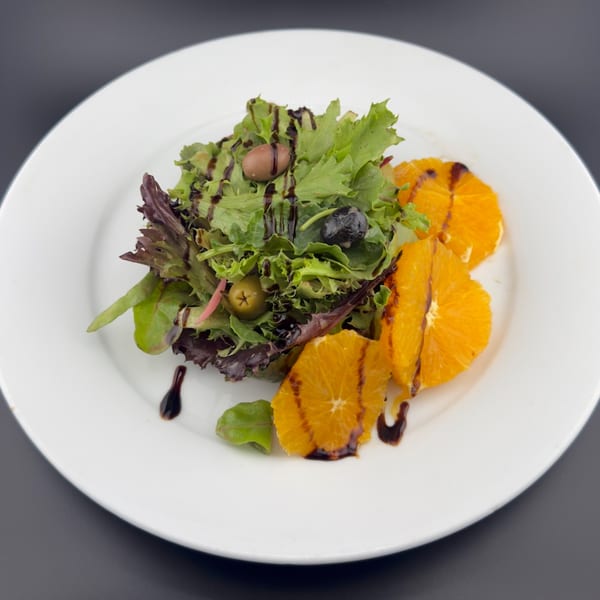 Fresh green salad with olives, orange slices, and balsamic glaze on a white plate.
